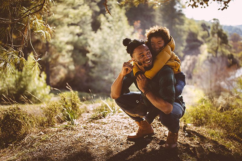 Father and son having fun with piggyback ride in forest